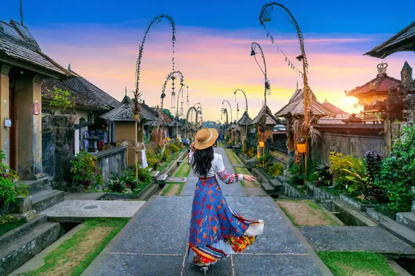 Woman in traditional attire walking through a Balinese village at sunset.
