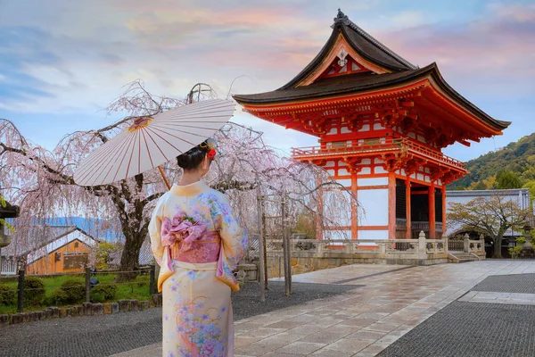 Woman in traditional kimono at a Japanese temple with cherry blossoms.